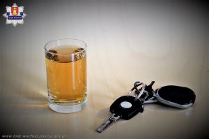 na blacie stoi szklanka z alkoholem i kluczyki od samochodu. W lewym górnym rogu logo koluszkowskiej komendy