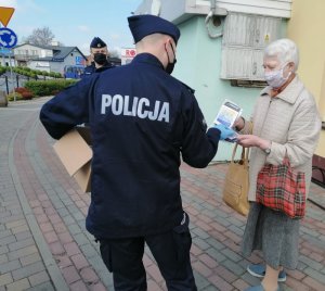 Umundurowany policjant rozdaje kobiecie maseczkę ochronną