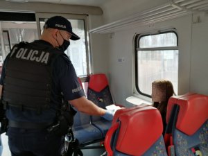 Umundurowany policjant podaje maseczkę ochronną pasażerce pociągu