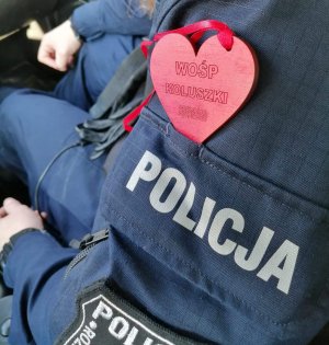 Czerwone serduszko z napisem WOŚP Koluszki włożone do kieszeni na ramieniu policyjnego munduru