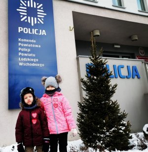 dwójka dzieci stoi przed budynkiem Komendy Powiatowej Policji powiatu łódzkiego wschodniego, dzieci na kurtkach mają przyklejone serduszka WOŚP