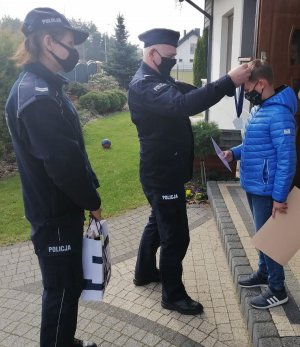 umundurowany policjant i policjantka wręczają nagrody chłopcu