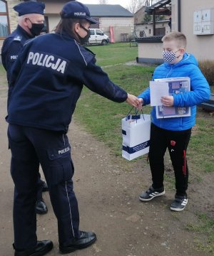 umundurowany policjant i policjantka wręczają nagrody chłopcu
