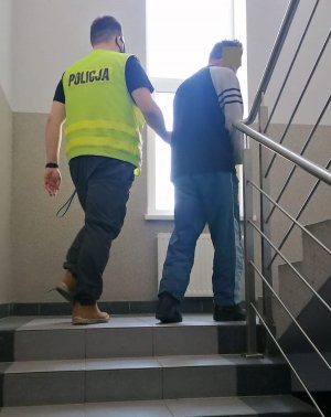 nieumundurowany policjant w żółtej kamizelce prowadzi po schodach zatrzymanego mężczyznę