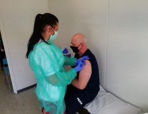 umundurowany policjant z maseczką na twarzy jest szczepiony przez pielęgniarkę