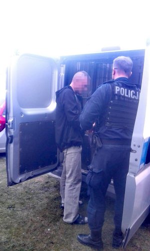 umundurowany policjant odwrócony tyłem stoi przy radiowozie z zatrzymanym mężczyzną