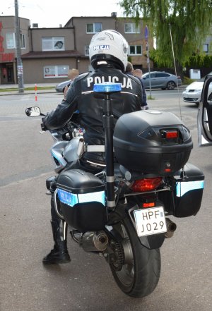 umundurowany policjant z białym kaskiem na głowie  siedzi na motorze odwrócony tyłem