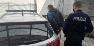 Policjant umundurowany prowadzi zatrzymanego mężczyznę do radiopwozu