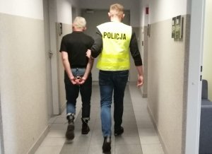 policjant w żółtej kamizelce z napisem policja prowadzi zatrzymanego mężczyznę