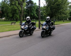 umundurowani policjanci w białych kaskach na głowach jadą na policyjnych motocyklach i jadą ulicą