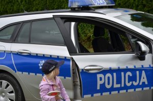dziecko stoi przy radiowozie a przy drzwiach samochodu stoi umundurowany policjant