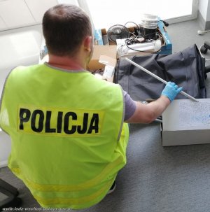 policjant w żółtej kamizelce z napisem policja odwrócony tyłem ogląda przedmioty