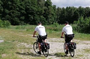 umundurowani policjanci jadą rowerami w stronę lasu