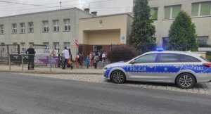 radiowóz policyjny stoi przy wejściu do szkoły, ze szkoły wychodzą dzieci