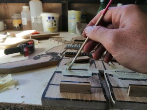 dłoń mężczyzny trzyma pędzelek do malowania i maluje na kawałku drewna