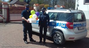 policjant z policjantką stoją przy radiowozie i trzymają pudełko z balonami