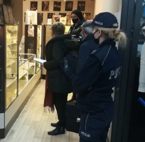 policjantka stoi bokiem w drzwiach wejściowych do sklepu, w środku w sklepie stoją 3 osoby w maseczkach