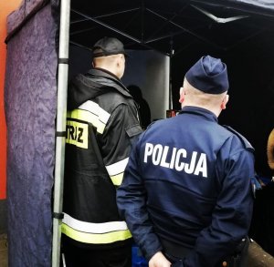 umundurowany policjant i strażak stoją odwróceni tyłem przy stoisku z fajerwerkami
