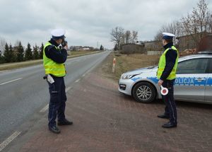 umundurowani policjanci stoją przy drodze i mierzą prędkość