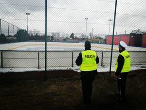 umundurowani policjanci w żółtych kamizelkach patrzą w stronę lodowiska, stoją przy samochodzie