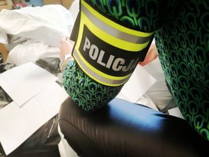 policjantka pochylona nad zabezpieczonymi ubraniami popakowanymi w worki, na lewym przedramieniu ma opaskę z napisem policja