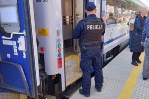 policjant stoi odwrócony tyłem przy stojącym pociągu