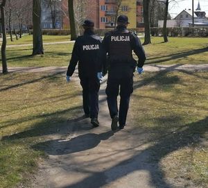 Umundurowani policjanci idą ścieżką w parku, są odwróceni tyłem
