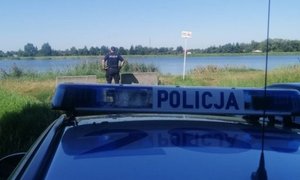 policjant stoi na brzegu zbiornika i patrzy przed siebie, stoi odwrócony tyłem, za nim stoi zaparkowany radiowóz
