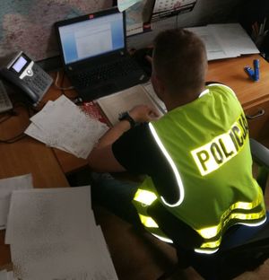 policjant w żółtej kamizelce z napisem policja siedzi przy biurku przed komputerem