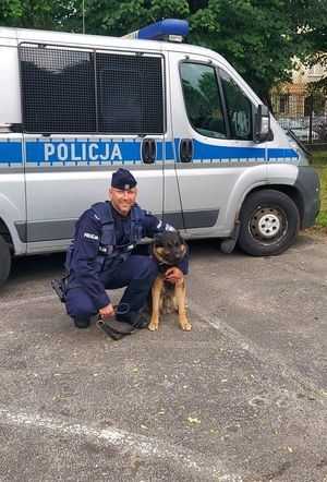 Policjant z psem stoi przy  radiowozie