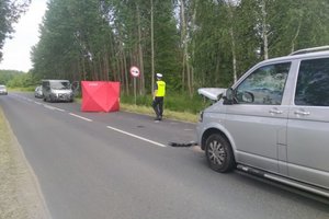 policjant w żółtej kamizelce i białej czapce na głowie stoi na drodze przy miejscu wypadku drogowego