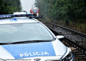 radiowóz policyjny stoi przy torach na których jedzie pociąg