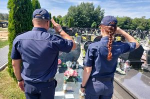 Policjanci stoją przed grobem zmarłych i oddają hołd