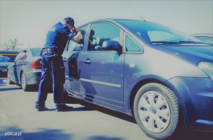 policjant stoi przy samochodzie i zagląda przez szybę
