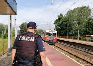 Policjant stoi przy torach kolejowych którymi jedzie pociąg