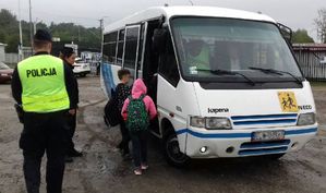 Policjanci stoją przy dzieciach wchodzących do autobusu szkolnego