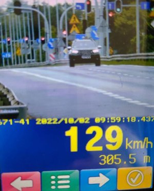 ekran wskazujący pomiar prędkości jadącego samochodu, w tle widać znaki drogowe i sygnalizatory świetlne