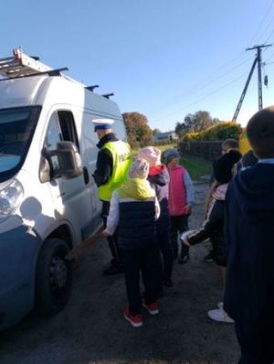 policjant wraz z dziećmi kontroluje kierowcę białego samochodu
