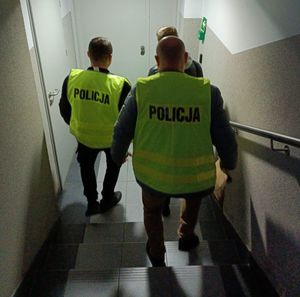 policjanci w żółtych kamizelkach z napisem policja prowadzą zatrzymanego mężczyznę