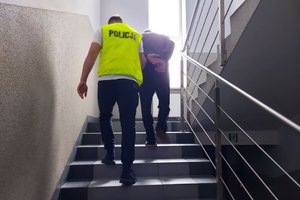 policjant w żółtej kamizelce prowadzi po schodach w górę zatrzymanego mężczyznę