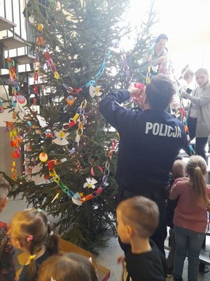 policjanci stoją przy choince i dekorują ją z dziećmi