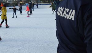 Policjant na tle lodowiska na którym na łyżwach jeżdżą dzieci