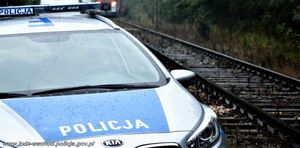 Radiowóz policyjny stojący przy torach kolejowych.