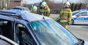 strażaqcy stoją przy rozbitym samochodzie, w tle policyjny radiowóz stoi