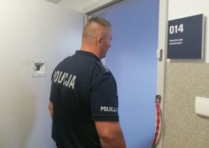 Policjant w granatowym mundurze stoi w wejściu do pomieszczenia przy otwartych metalowych drzwiach