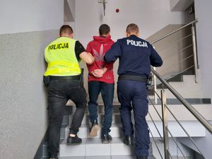 Dwóch policjantów prowadzi po schodach w górę zatrzymanego mężczyznę.