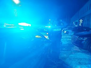 Policjanci stoją przy radiowozach z migającymi niebieskimi światłami.