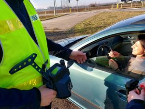 Policjant podaje kobiecie siedzącej za kierownicą zawieszkę w kształcie serduszka.