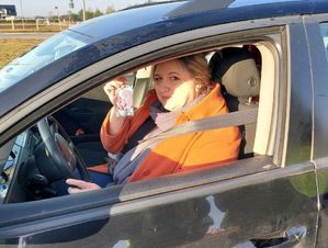 Kobieta siedząca za kierownicą pokazuje trzymane w dłoni serduszko.
