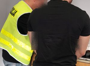 Policjant w żółtej kamizelce z napisem policja pobiera odciski palców od mężczyzny stojącego obok niego.